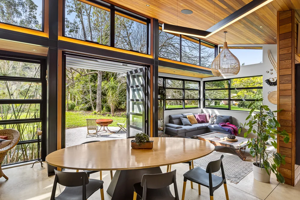 Open-plan living and dining with bush views in an Auckland home built by Baker Brothers Construction
