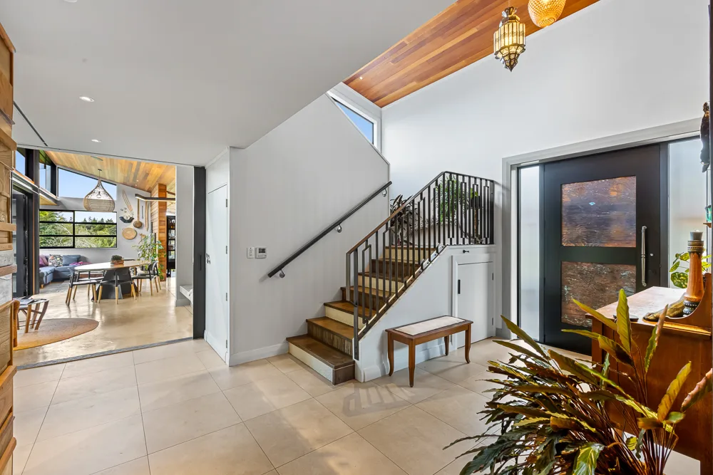 Auckland entry hall with timber staircase, black steel balustrade, cedar ceiling detail and open outlook through to the living area