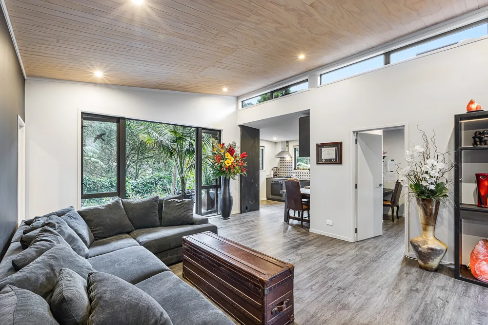 Auckland living area with timber-lined ceiling and high clerestory windows, opening through to a kitchen and dining space