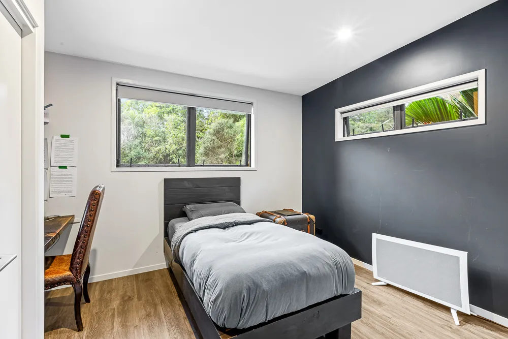 Auckland bedroom and study nook with navy feature wall, awning window to native bush and a built-in desk area